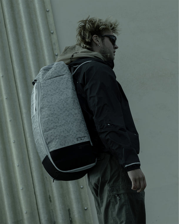 Side view of a man wearing the Db Hugger Bootpack 45L backpack in White Noise.
