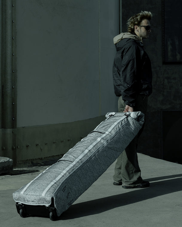 Db Snow Roller Pro 127L ski bag in White Noise wheeled outdoors by a traveler.