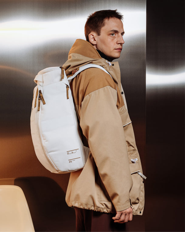 Man wearing the Db Hugger 25L Backpack in Oatmilk with a tan outdoor jacket.
