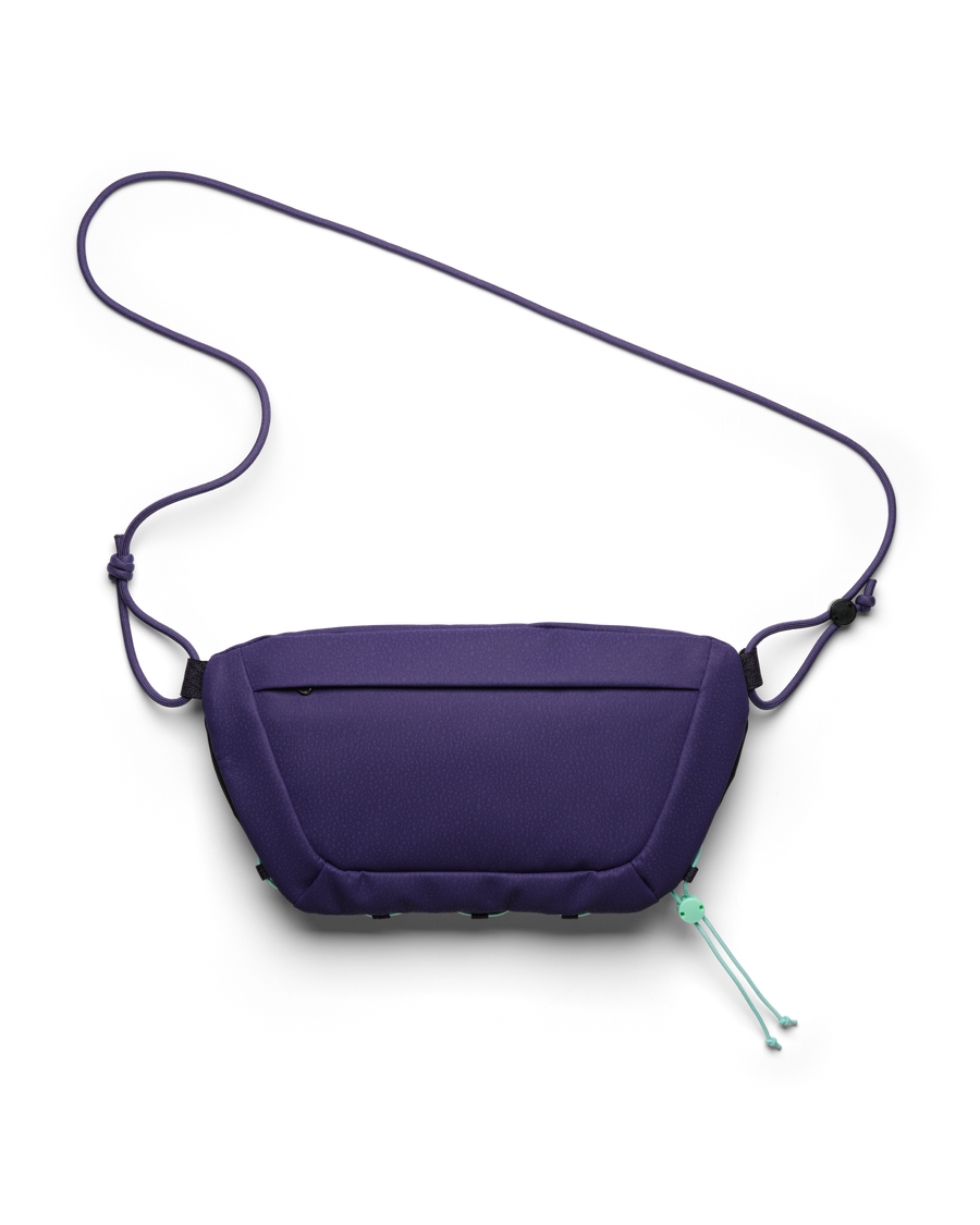 Back view of the Db Roamer Pro Sling Bag 6L in purple with cord shoulder strap and zipper pocket.